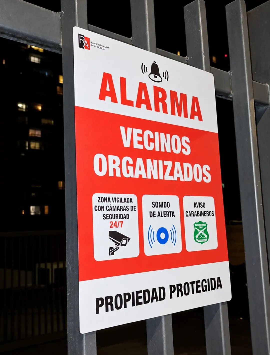 Letrero «Alarma vecinos organizados · Propiedad protegida» instalado en una reja